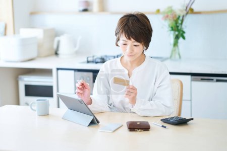 Photo for A woman holding a card and operating a tablet PC in the room - Royalty Free Image