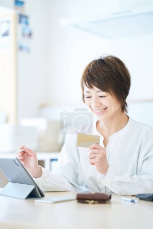 Foto de Una mujer sosteniendo una tarjeta y operando una tableta PC en la habitación - Imagen libre de derechos