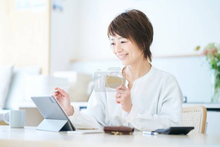 Photo for A woman holding a card and operating a tablet PC in the room - Royalty Free Image