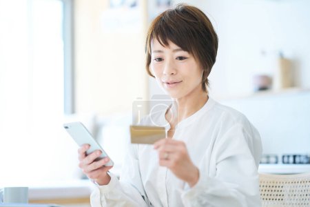 Foto de Una mujer sosteniendo una tarjeta y operando un teléfono inteligente en la habitación - Imagen libre de derechos
