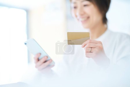 Téléchargez les photos : Une femme tenant une carte et opérant un smartphone dans la chambre - en image libre de droit