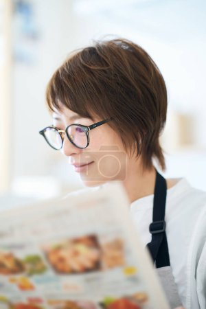 Téléchargez les photos : Une femme portant des lunettes regardant une brochure publicitaire dans la chambre - en image libre de droit