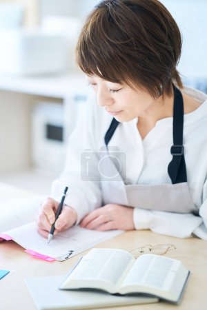 Foto de Una mujer en un delantal estudiando por texto en la cocina - Imagen libre de derechos