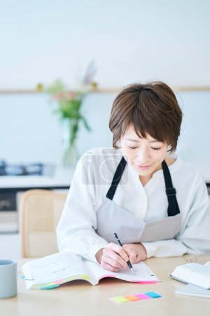 Photo for A woman in an apron studying by text at kitchen - Royalty Free Image