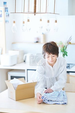 Téléchargez les photos : Femme tenant des vêtements sur la table dans la chambre - en image libre de droit