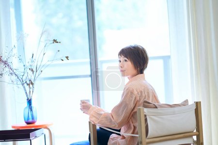 Photo for Woman relaxing by the window in her room - Royalty Free Image