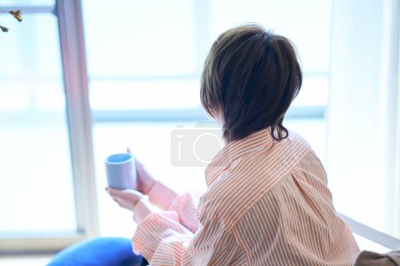Téléchargez les photos : Femme relaxante près de la fenêtre dans sa chambre - en image libre de droit