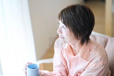 Téléchargez les photos : Femme relaxante près de la fenêtre dans sa chambre - en image libre de droit