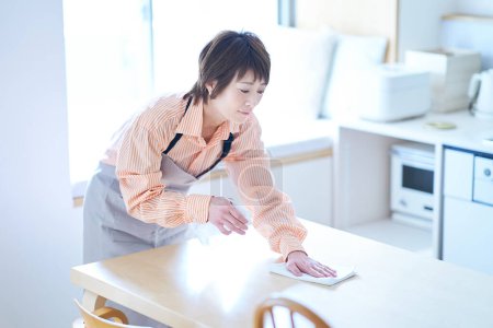 Téléchargez les photos : Femme essuyant la table à manger dans la chambre - en image libre de droit