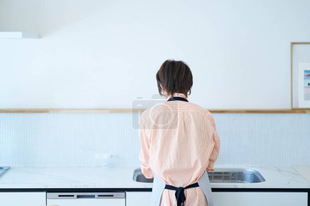 Téléchargez les photos : Vue arrière d'une femme qui lave la vaisselle dans la cuisine - en image libre de droit