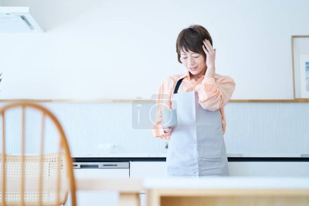 Photo for A woman in an apron who suffers from a headache in the room - Royalty Free Image