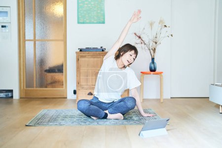 Photo for A woman stretching in a room while looking at a tablet PC screen - Royalty Free Image