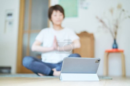 Téléchargez les photos : Une femme s'étirant dans une pièce en regardant un écran de tablette PC - en image libre de droit