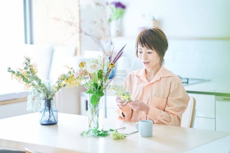 Téléchargez les photos : Femme arrangeant des fleurs avec vase à fleurs dans la chambre - en image libre de droit