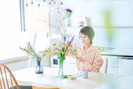 Foto de Mujer arreglando flores con florero en la habitación - Imagen libre de derechos