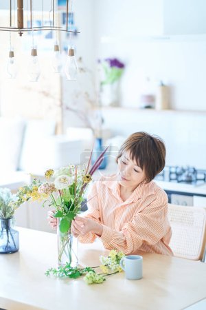 Téléchargez les photos : Femme arrangeant des fleurs avec vase à fleurs dans la chambre - en image libre de droit