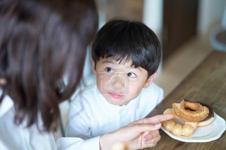 Téléchargez les photos : Mère et fils manger beignet à la maison - en image libre de droit