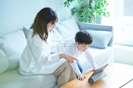 Téléchargez les photos : Mère et enfant assis sur le canapé et regardant l'écran de la tablette PC - en image libre de droit