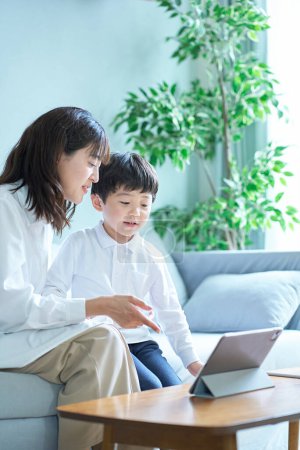 Téléchargez les photos : Mère et enfant assis sur le canapé et regardant l'écran de la tablette PC - en image libre de droit