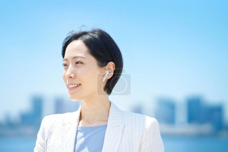 Photo for Woman in a suits wearing wireless earphones outdoors - Royalty Free Image