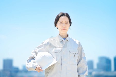 Téléchargez les photos : Une femme en vêtements de travail tenant un casque le beau jour - en image libre de droit