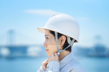 Téléchargez les photos : Une femme portant des vêtements de travail et vérifiant un casque le beau jour - en image libre de droit