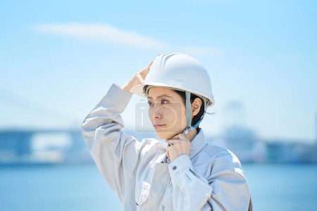 Foto de Una mujer vestida con ropa de trabajo y revisando un casco en un buen día - Imagen libre de derechos