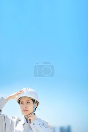 Téléchargez les photos : Une femme portant des vêtements de travail et vérifiant un casque le beau jour - en image libre de droit