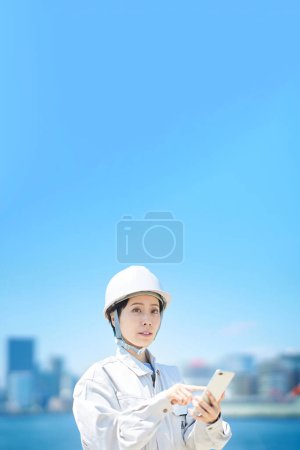 Foto de Una mujer con ropa de trabajo sosteniendo un teléfono inteligente en un buen día - Imagen libre de derechos
