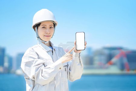Téléchargez les photos : Une femme en tenue de travail tenant un smartphone le beau jour - en image libre de droit