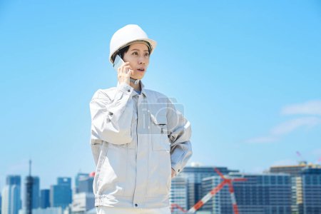 Foto de Una mujer en ropa de trabajo hablando en un teléfono inteligente en un buen día - Imagen libre de derechos