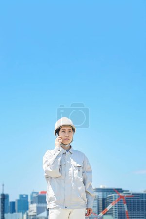Foto de Una mujer en ropa de trabajo hablando en un teléfono inteligente en un buen día - Imagen libre de derechos