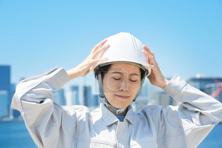 Téléchargez les photos : Une femme en vêtements de travail tenant sa tête à l'extérieur - en image libre de droit