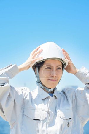 Photo for A woman in work clothes holding her head outdoors - Royalty Free Image