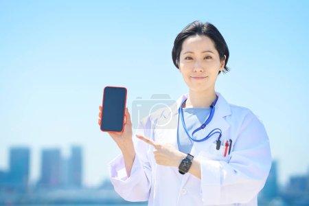 Téléchargez les photos : Une femme en manteau blanc avec un smartphone le beau jour - en image libre de droit