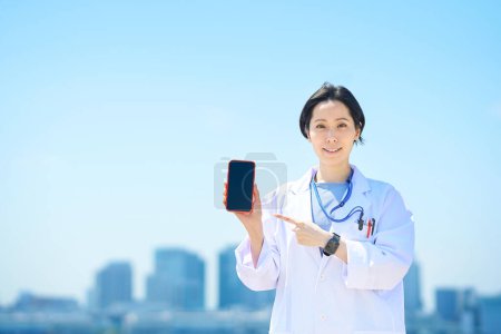 Photo for A woman in a white coat with a smartphone on fine day - Royalty Free Image