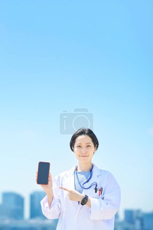 Photo for A woman in a white coat with a smartphone on fine day - Royalty Free Image