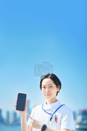 Téléchargez les photos : Une femme en manteau blanc tenant un smartphone à l'extérieur - en image libre de droit