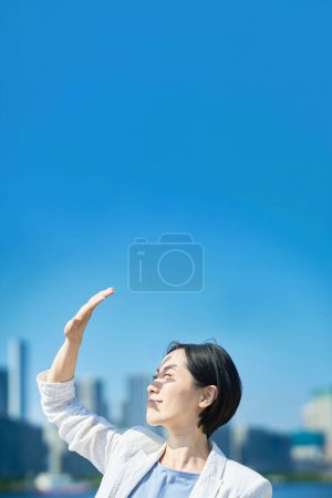 Téléchargez les photos : A woman blocking the strong sunlight with her hand on fine day - en image libre de droit