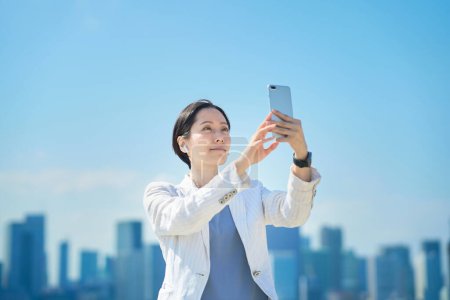 Téléchargez les photos : Asiatique femme tenant un smartphone à l'extérieur - en image libre de droit
