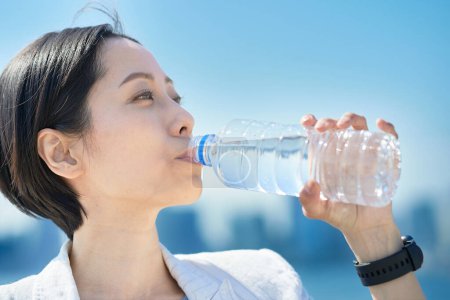 Téléchargez les photos : Femme eau potable à partir d'une bouteille en plastique à l'extérieur - en image libre de droit