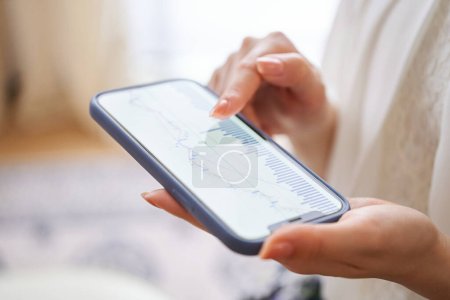 Photo for A woman's hand checking the exchange chart on her smartphone in the room - Royalty Free Image