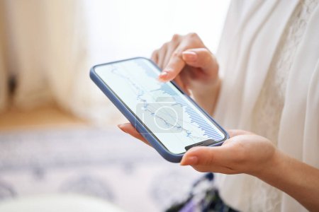 Téléchargez les photos : Une main de femme vérifie le tableau d'échange sur son smartphone dans la chambre - en image libre de droit