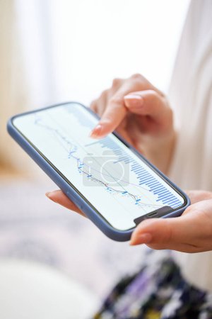 Photo for A woman's hand checking the exchange chart on her smartphone in the room - Royalty Free Image