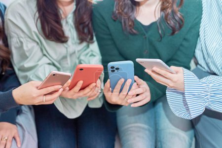 Foto de Cuatro mujeres hablando mientras miran sus teléfonos inteligentes en el interior - Imagen libre de derechos