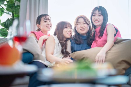 Foto de Cuatro mujeres jóvenes relajándose en una fiesta en casa - Imagen libre de derechos