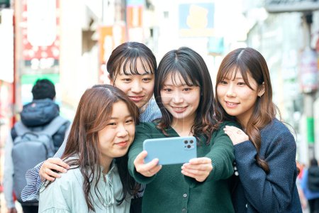 Téléchargez les photos : Quatre femmes prennent volontiers des selfies dans la ville - en image libre de droit