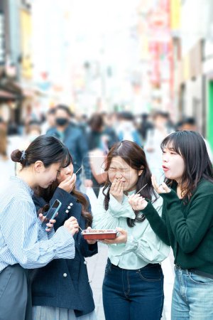 Téléchargez les photos : Quatre femmes mangent et marchent au centre-ville - en image libre de droit