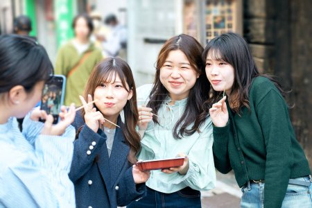 Photo for Four women walking around eating takoyaki in the downtown area - Royalty Free Image