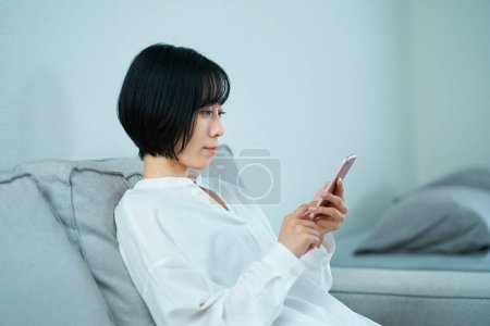Photo for Woman sitting on sofa and using smartphone in the room - Royalty Free Image